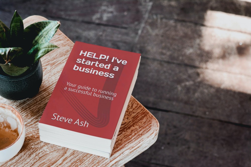 A book called HELP! I've Started A Business lying on a wooden table next to a pot plant